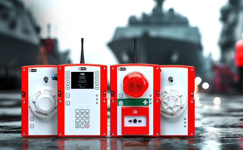 WES3-units van ASG Fire-Alert op een vochtige scheepswerf: Connect-bedieneenheid, handbrandmelder met rood flitslicht en draadloze detectoren, met grijze schepen op de achtergrond